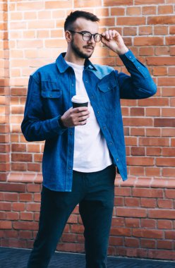 Günlük kıyafetleri içinde beyaz tenli genç adam sokakta duran gözlüklere bakıyor, sakallı erkek kahve içiyor ve boş zamanlarını dışarıda geçiriyor.