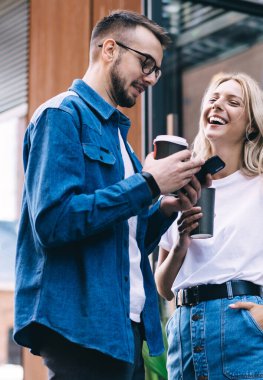 Neşeli beyaz kadın, erkek arkadaşının cep telefonunun birlikte vakit geçirmesinin komik medya içeriğine gülüyor. Erkek, elinde cep telefonu ile sosyal ağdan kadın kolejine video gösteriyor.