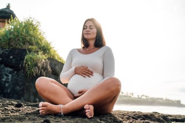 30 'lu yaşların sonlarında anne adayı deniz kenarında meditasyon yapıyor. Huzur ve anne güzelliği yayıyor. Huzurlu bir yoga inzivasında.