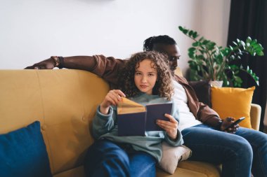 Kıvırcık saçlı, rahat elbiseli, kendine güveni tam genç bir eş. Kanepede oturup, ilginç kitaplar okurken, aynı zamanda evinde rahat bir oturma odasında, akıllı telefonları karıştırıyor.
