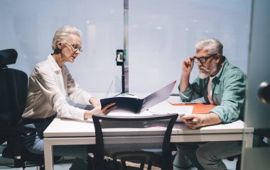 Modern ofis ortamındaki belgeler üzerine odaklanmış Kafkas iş arkadaşları. Dizüstü bilgisayarı olan beyaz bluzlu bir kadın, gözlüklü bir adam.