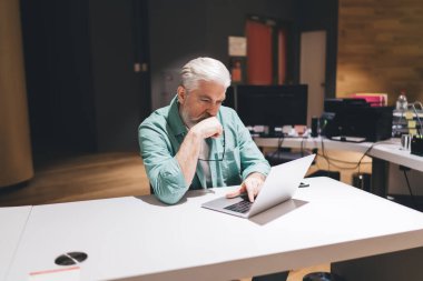 Çağdaş ofis ortamında dizüstü bilgisayarla çalışan düşünceli üst düzey beyaz adam, konsantrasyon, problem çözme ve sürekli profesyonel gelişim kavramını yansıtıyor..