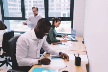 Bir grup pozitif, çok ırklı iş adamı, aydınlık ofis odasında çalışırken dizüstü bilgisayar ve belgelerle masada oturuyorlar.