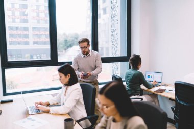 Çağdaş ofis odasında çalışma saatlerinde masada otururken bilgisayarlarla birlikte çalışan ve verileri analiz eden çeşitli iş arkadaşları.