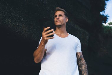 Akşamları gözlerini kaçırırken Dark Rock 'ın yanında dikilen sıradan giyinmiş ciddi genç bir erkeğin düşük açılı portresi.