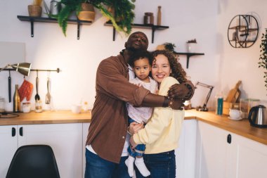 Sevimli küçük kızı olan çeşitli anne babalar mutfak tezgahında oturup modern apartmanda birlikte vakit geçirirken birbirlerine sarılıyorlar.