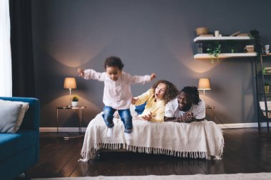 Afrika kökenli sevimli bir kız. Şaşırmış ve korkutucu ebeveynleriyle birlikte yataktan atlıyor. Modern dairenin aydınlık yatak odasında rahat bir yatakta uzanıyor.