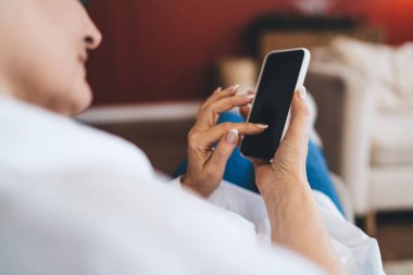 Tanımlanamayan bir kadının kanepede dinlenmesi ve evde bulanık oturma odasında boş zamanlarında cep telefonu ekranına bakarken parmaklarıyla göz atması.