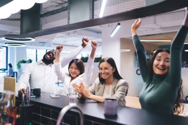 Tezgahta oturan, el ele tutuşan ve iş yerinde elde edilen başarıları kutlayan ve içki içen çok ırklı meslektaşlardan oluşan bir grup.