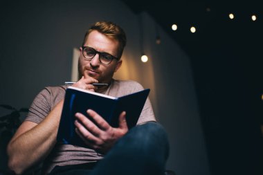 Ciddi bir erkek öğrenci eğitim kitabında not edilen bilgileri kontrol ediyor, optik gözlüklü akıllı adam blogcu göz düzeltme içeriği okuma planı için telif defterinde - yaratıcı zaman