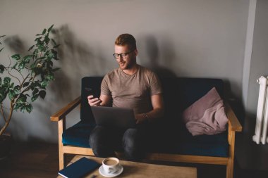 Optik gözlüklü milenyum erkek programcısı, bluetooth kullanarak bilgisayar ve akıllı telefon teknolojisiyle cep telefonuyla medya dosyalarını paylaşıyor.