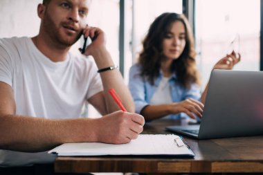 Bulanık erkek ve kadın serbest çalışanlar modern teknolojiyi iş planlaması için kullanıyorlar. Milenyum adamı cep telefonuyla gazetecilik notları yazarken kadın programcıIık yapıyor.