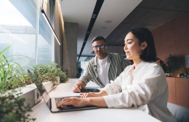 İş birliği sırasında yeni başlatılan proje için modern dizüstü bilgisayarda uygulama kullanan yetenekli erkek ve kadın meslektaşlar, internet üzerinden internet üzerinden bilgi işleme uzmanları web sitesi