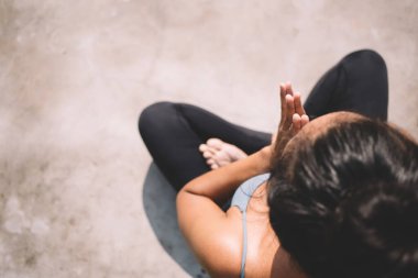 Spor kıyafetleri içinde tanınmayan bir bayanın Lotus pozunda otururken ellerini sımsıkı tutması ve yoga seansında farkındalık çalışması.