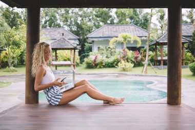 Yazın çıplak ayaklı, gülümseyen genç kadın çalışanın yan görünüşü bilgisayarla uzaktan kumandalı bir projede çalışırken akıllı telefon takınıyor.