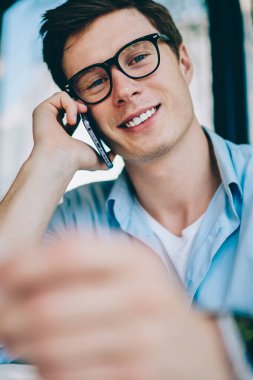 Gözlük vizyon düzeltme smartphone aygıtında çağrılırken kameraya gülümseyen pozitif genç adam portresi. Neşeli hipster öğrenci telefonla iş vacancy hakkında konuşmak