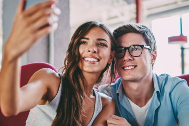Gülüyor ve selfie alan coworking içinde sınava hazırlık sırasında modern smartphone yapma olumlu hipster öğrenci. Mutlu çift ön kamera telefon ve blog alarak fotoğraf gülümseyen aşık