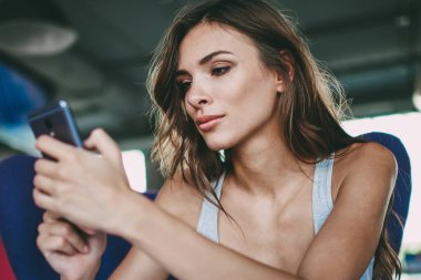 Dalgın hipster blogger kafede oturan ve ücretsiz Wi-Fi bağlantısını kullanarak modern smartphone üzerinde kendi blog yorumlar okuma. Genç kadın online sosyal ağlar üzerinde cep video izlerken konsantre