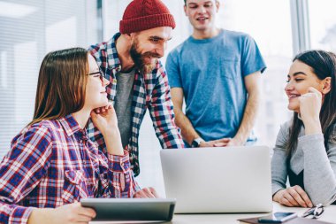 Başarılı grup genç profesyonellerin rahat kıyafet laptop ofiste oturan tasarım proje üzerinde işbirliği sırasında gülüyor. Beyin fırtınası sırasında ortak görev üzerinde olumlu öğrenciler teamworking