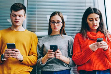 Duvara yakın duran ve akıllı telefonlar üzerinde online sohbet mesajlaşma dalgın hipster blogcular. Canlı iletişim görmezden sosyal ağlardan bağımlısı rahat kıyafet bin yıllık gençlerin antisosyal