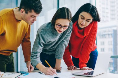 Takım içinde çalışma ve çizim dalgın hipster öğrenciler ayakta üzerinden masaüstü ofis içinde laptop ile kroki. Genç kadın beyin fırtınası toplantısı meslektaşları ile iş projesi için notları yazma