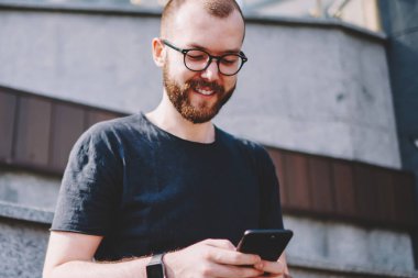 Neşeli sohbet online sosyal ağlar üzerinde modern smartphone ücretsiz 4 g kullanarak Eyewear genç adam sakallı Internet. Pozitif hipster blogger arkadaş dijital hücresel mesajlaşma süre gülüyor