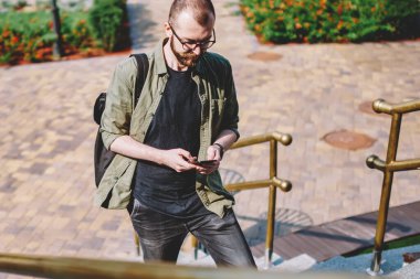Kentsel ortamda merdivenlerde geziniyor smartphone aygıtında SMS mesajı yazarak erkek blogger rahat giyinmiş. Genç adam online telefon aygıtı 4 g kullanarak sokakta yürürken sohbet internet
