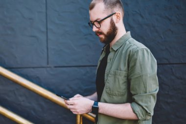 Hücresel üst katta devam app yükleme Hipster adam rahat kıyafet profil sayfası modern smartphone açık havada, yürüyüş 4 g internet bağlantısı kullanarak güncelleştirme dalgın genç adam blogger giymiş