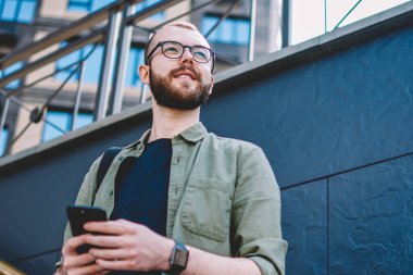 Aşağıda görünümü düşünceli erkek blogger düşünce modern smartphone kentsel ortamda merdivenlerde açık havada duran üzerinde internet yayıncılığı. Düşünceli hipster adam uzakta süre irsal sms arıyorsunuz