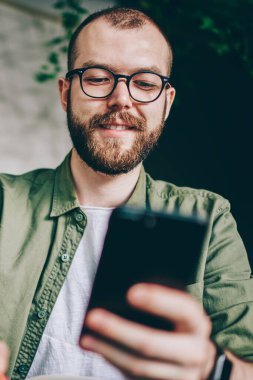 Aşağıda pozitif görünümü kullanarak 4 g Smartphone cep telefonu ile takipçileri komik bildirim okunurken gülen genç adam sakallı Internet. Video izlerken gülmekten gözlük neşeli hipster adam