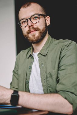 Akıllı telefon ve internet web sitesi için arama bilgileri kullanarak ödev sakallı yetenekli öğrenci portresi. Kahve masada oturan ve notlar aşağı yazma dijital cep telefonunuzla genç adam