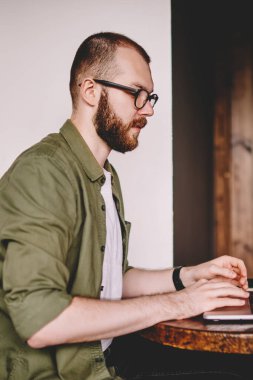 Dalgın genç adam serbest meslek bilgi modern dizüstü bilgisayar aygıtının kahve dükkanında kablosuz Internet bağlantısı kullanarak klavye yazarak yan görünüm. Uzaktan çalışma dijital netbook hipster öğrenci