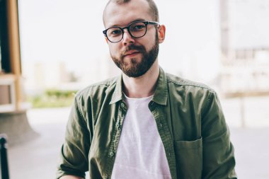 Serbest, genel 4 g kullanarak dizüstü bilgisayar üzerinde çalışırken kameraya bakarak gözlük sakallı genç adam portresi Internet. Mesafe işi sırasında netbook ile sokakta oturan hipster adam