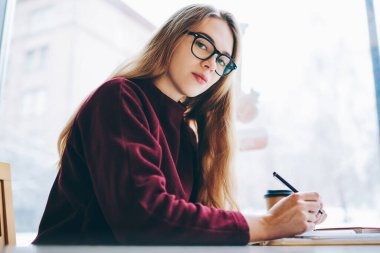 Kafede masada oturan ve eğitim, kamera kapalı, öğrenme tatilinde bakarak güzel hippi kız ciddi kız öğrenci portresi organizasyon planı yazma kadın çekici