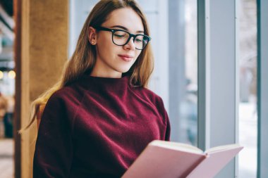 Olumlu kitap kapalı okuma başarılı kız öğrenci giyim gözlük vizyon düzeltme Üniversitesi kafeterya, beyaz akıllı hippi kız rahat edebiyat zevk için giyinmiş