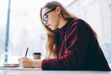 Konsantre genç akıllı yazar giyim moda gözlük kahve dükkanında otururken yeni makaleler oluşturma içinde kız öğrencinin sınav düşünme üzerinde kapalı soru için cevap için hazırlanıyor durulması