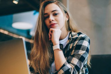 Portre rahat giyinmiş öğrenci oturma masaüstü netbook Üniversitesi kafeterya, kapalı, yeni dizüstü bilgisayar üzerinde çalışmaya ara kameraya bakarak çekici kadın yazılım geliştirici