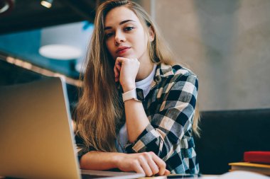 Portre rahat giyinmiş öğrenci oturma masaüstü netbook Üniversitesi kafeterya, kapalı, yeni dizüstü bilgisayar üzerinde çalışmaya ara kameraya bakarak çekici kadın yazılım geliştirici