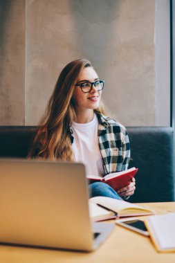 Pozitif gülümseyen hippi kız giyim gözlük vizyon düzeltme bilgisayarı kullanmak ve sınav için hazırlanıyor süre uzağa arıyorsunuz ve bekleyen arkadaş kitap okuma coworking uzay zaman geçirmek için