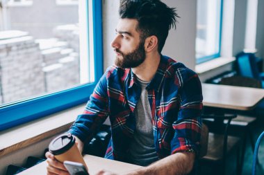 Düşünceli hipster adam arkadaş çağrı için yeni smartphone bekliyor ve kafein içecek, dalgın adam holding cep telefonu ve fincan kahve kapalı zevk kafeterya penceresine bakarak