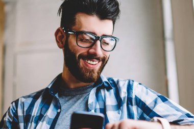 Gülümseyen başarılı hipster adam elinde Üniversitesi kampüsünde, mutlu bir adam tutarak mobil telefon toplantı ve kol saati mesajı okuma için beklenirken giyilebilir smartwatch zamanında kontrol Eyewear