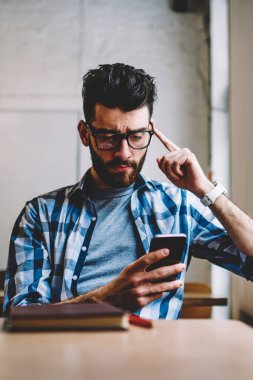 Genç iş üstünde hareket eden telefon, wifi kapalı bağlı modern smartphone cep telefonu ile dosya indirme konsantre erkek blogger uygulamasını kullanarak kısa mesaj okuma gözlüğü hipster adam karıştı