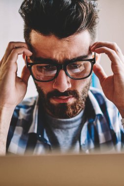 Genç beyaz erkek programcı son tarih içinde yazıhane bilgisayar, şaşkın şaşkın hipster adam kötü haber için wifi bağlıyken modern netbook üzerinde okuma ile deckstop oturan baş ağrısı hissediyor