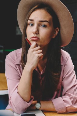 Genç kadın şık şapkalı kahve masada oturan yarım uzunluk portre. Kafeteryada istirahat ederken kameraya el arıyorum kalem ile mutsuz hippi kız. Kötü ruh ile sevimli kadın blogger