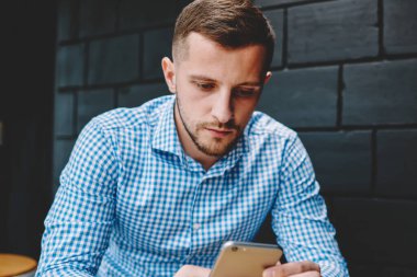 4 g internet bağlantısı kullanarak modern smartphone aygıt üzerindeki mali haber okuma dalgın genç adam. Hippi erkek blogger sohbet ve kafe iç oturan telefonu dosya indirme