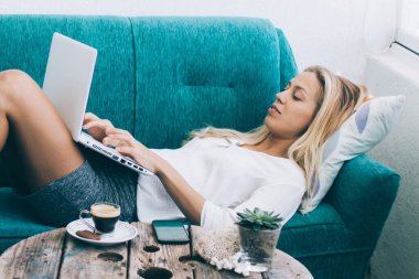 Çekici kadın serbest meslek sahibi Webinar sırasında rahat koltukta yalan ev iç, Genç beyaz kadın blogger boş zamanlarında netbook üzerinde online ve tebliğ ile sokulgan yolu ile dizüstü cihaz izlerken