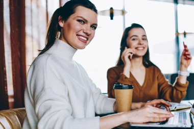 Kafeterya wifi, kahve dükkanında netbook üzerinde Internet tarama birlikte vakit iki kadın blogcular kullanarak dizüstü aygıtı ile masaüstünde oturan gülümseyen bin yıllık kadın metin yazarı portresi