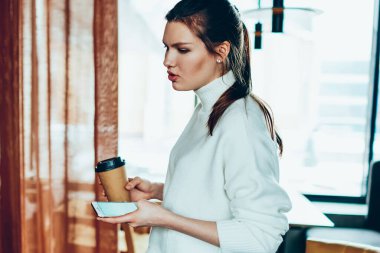 Bin yıllık kadın serbest kafeterya, akıllı telefon tutarak ve arkadaşına nasıl kontrol dizüstü bilgisayarda güncelleştirmeleri açıklayan genç ciddi kadın kahve molası sırasında ekip çalışması için fikirler tartışıyor