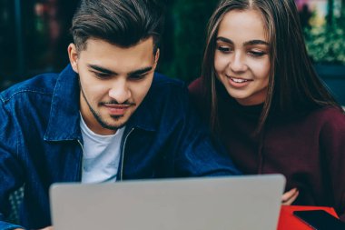 Genç kadın ve erkek öğrenciler dizüstü bilgisayarda birlikte Café, rezervasyon yapmak internet bağlantısı ile birlikte memnun üstünde örümcek ağı sayfa yolu ile netbook hipster çift wifi kullanarak öğretici izlerken
