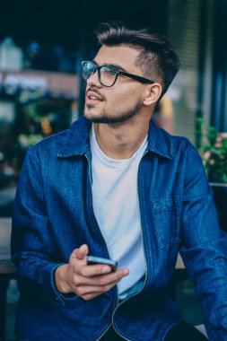 Rüya gibi yenilikçi adam fikir blogu Café, gözlük el kablosuz internet'e bağlanan uzak tutarak smartphone seyir dalgın yakışıklı adam cep telefonu kullanarak yazı için düşünüyorum